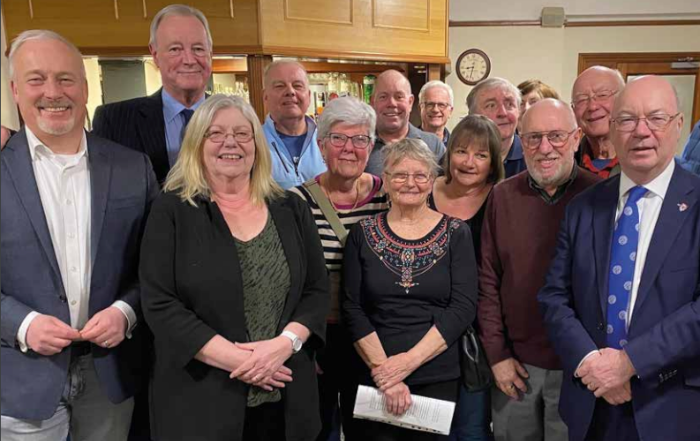 A group of tory club members stand together indoors, smiling at the camera in a casual setting.
