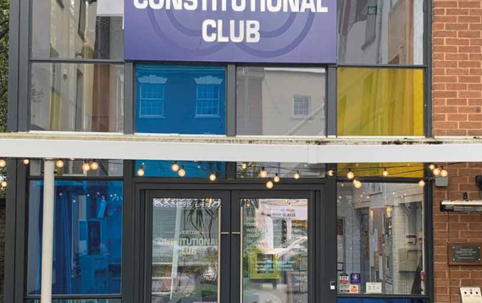 Entrance to Tiverton Constitutional Club with glass doors and a blue sign above.
