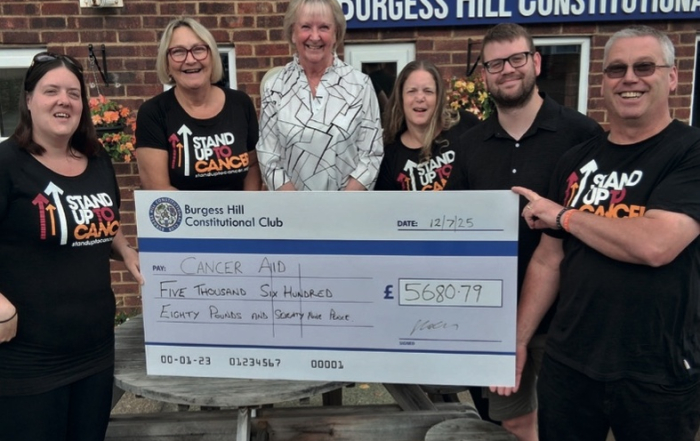 Six people pose with a large Cancer Aid donation cheque for £5,680.79 outside Burgess Hill Constitutional Club.
