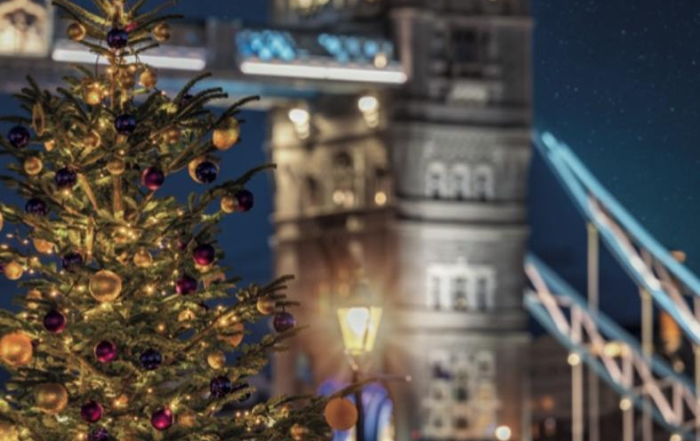 A decorated Christmas tree stands in front of Londons illuminated Tower Bridge at night.
