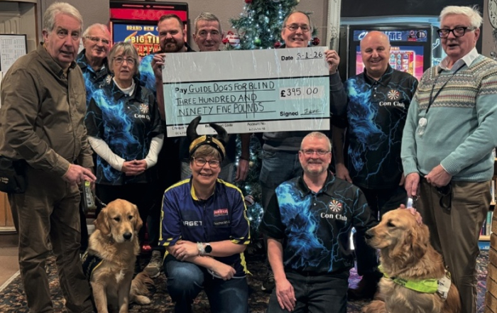 A group holding a large cheque for Guide Dogs for Blind for £395, with two guide dogs in front of a Christmas tree.